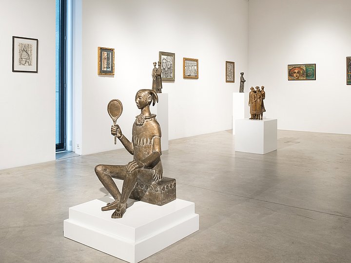Weißer Saal mit einer sitzenden Skulptur auf einem Sockel