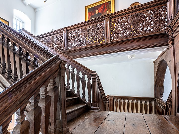 Treppenhaus mit geschnitztem Geländer, darüber ein Gemälde